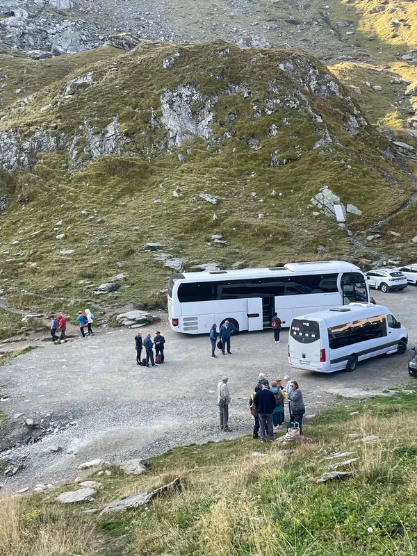 Turiști pe un platou montan stâncos, lângă autocarele excursiei